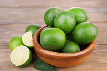 Fresh juicy limes in bowl on old wooden table