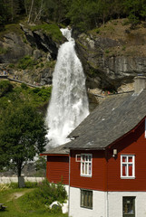 Fototapeta na wymiar steindalsfossen, rotes holzhaus und wasserfall in norwegen