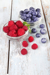 Glass bowls of raspberries and blueberries on wooden background