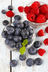 Glass bowls of raspberries and blueberries on wooden background