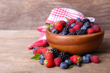 Ripe sweet different berries in bowl, on old wooden table