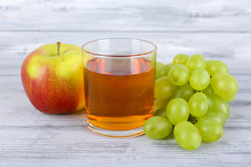 glass of juice with fresh grape and apple on grey wooden table