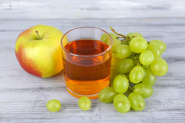 glass of juice with fresh grape and apple on grey wooden table
