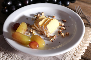 tasty grape and cheese on plate, on wooden table