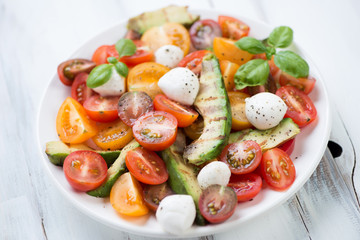 Plate with grilled avocado, tomatoes, mozzarella and basil salad