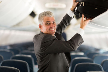 middle aged business traveler putting luggage into overhead lock