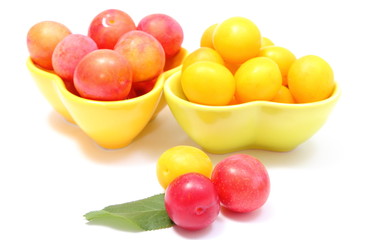Heap of red and yellow mirabelle in bowls. White background