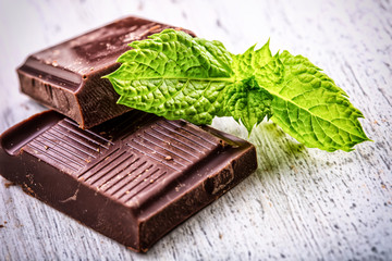 A few cubes of black chocolate with mint leaves on wooden table