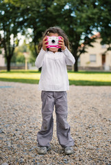 Portrait of young girl with digital compact camera outdoors.