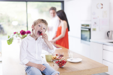 young boy eating  strawberries in family kitchen
