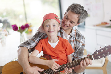 father learning his boy to play guitar