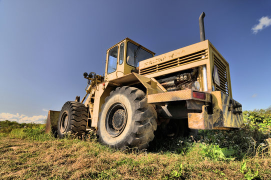Big yellow old loader standing abandoned in a grass