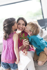 kids kissing their mother and offering a flower