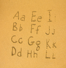 Alphabet written on a sand beach. (A-L)