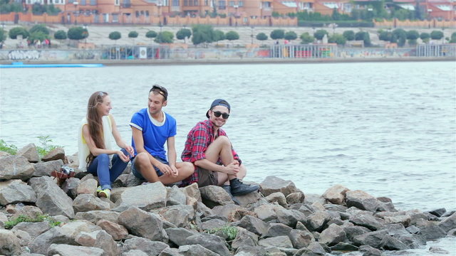 Three friends sitting and laughing on the rocks by the river
