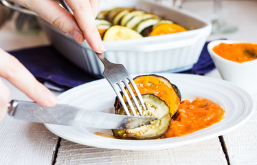 eat warm ratatouille in a round plate with a fork and knife, han