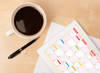 Tablet pc showing calendar on screen with a cup of coffee on a d