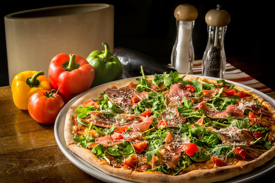 Pizza with rucola and Black Forest ham wooden table vegetables