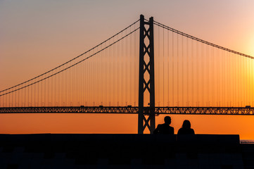 silhouette couple sitting together with bridge