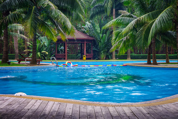 Swimming pool with hut and wooden pool deck in garden of resort