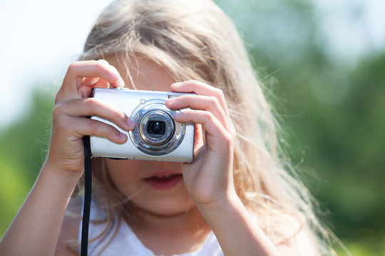 Young blond girl holding digital camera and photographing