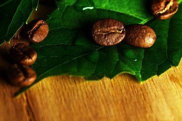 Beans of black coffee with fresh green leaves over wooden textur