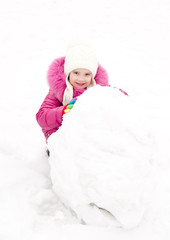 Cute smiling little girl makes snowman in winter day