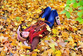 Woman portrait lying on autumn leaves in park.