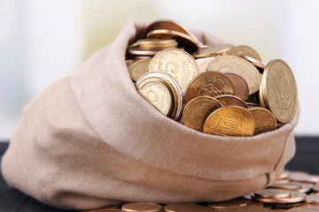 Fabric bag full of Ukrainian coins on wooden background