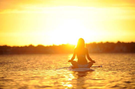 Frau macht SUP Yoga bei Sonnenuntergang