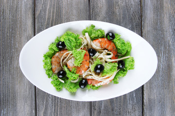 Fresh prawns with spaghetti, olives and lettuce in a white oval