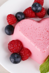 Heart shaped cake with berries on plate on wooden background