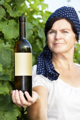 Woman holding bottle full of wine in vineyard