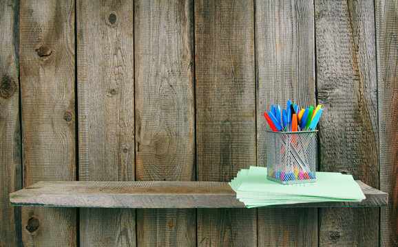 Pens and writing-books on a wooden shelf.