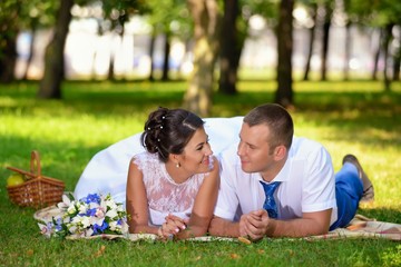 Fototapeta premium Happy bride and groom on their wedding lies on the grass in park