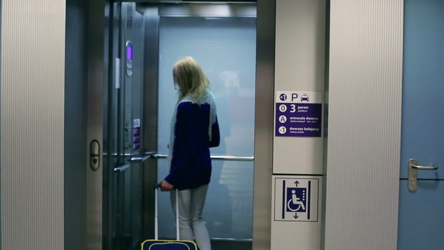 Young woman entering elevator and holding luggage