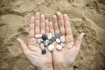 Stonesin female hands on a background of sand.