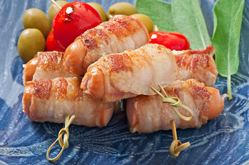 Grilled sausages wrapped in strips of bacon with tomatoes