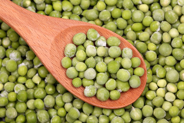 Frozen green peas in a wooden spoon