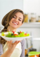 Portrait of happy young housewife showing salad