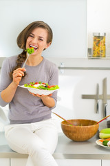 Happy young woman eating greek salad in modern kitchen