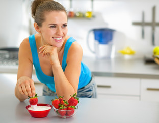 Happy young woman eating strawberry with yogurt