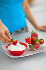 Closeup on happy young woman eating strawberry with yogurt