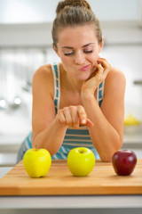 Thoughtful young woman choosing between red and green apples