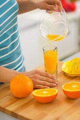 Closeup on young woman pouring fresh orange juice in glass