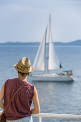 Fototapeta premium Female passenger on the deck of the ferry watching the sailboat