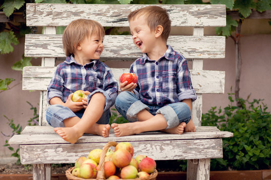 Two boys, sitting on a bench, eating apples and having fun