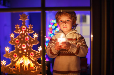 Obraz na płótnie Canvas Cute toddler boy standing by window at Christmas time and holdin