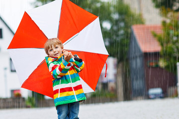 Smiling boy with yellow umbrella and colorful jacket outdoors at