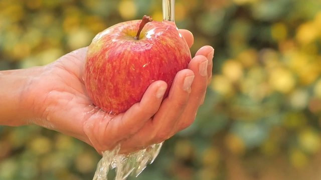 red apple in hand under flowing water slow motion